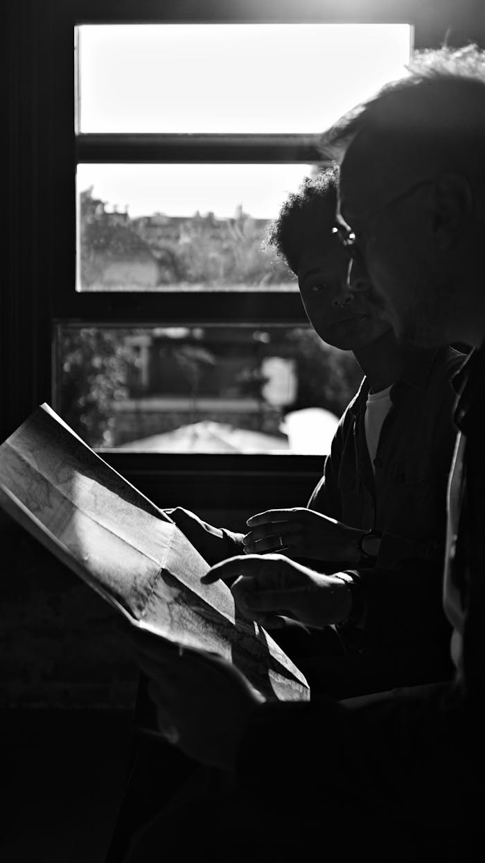 Two people study a map in a silhouette against a sunlit window, suggesting planning or exploration.