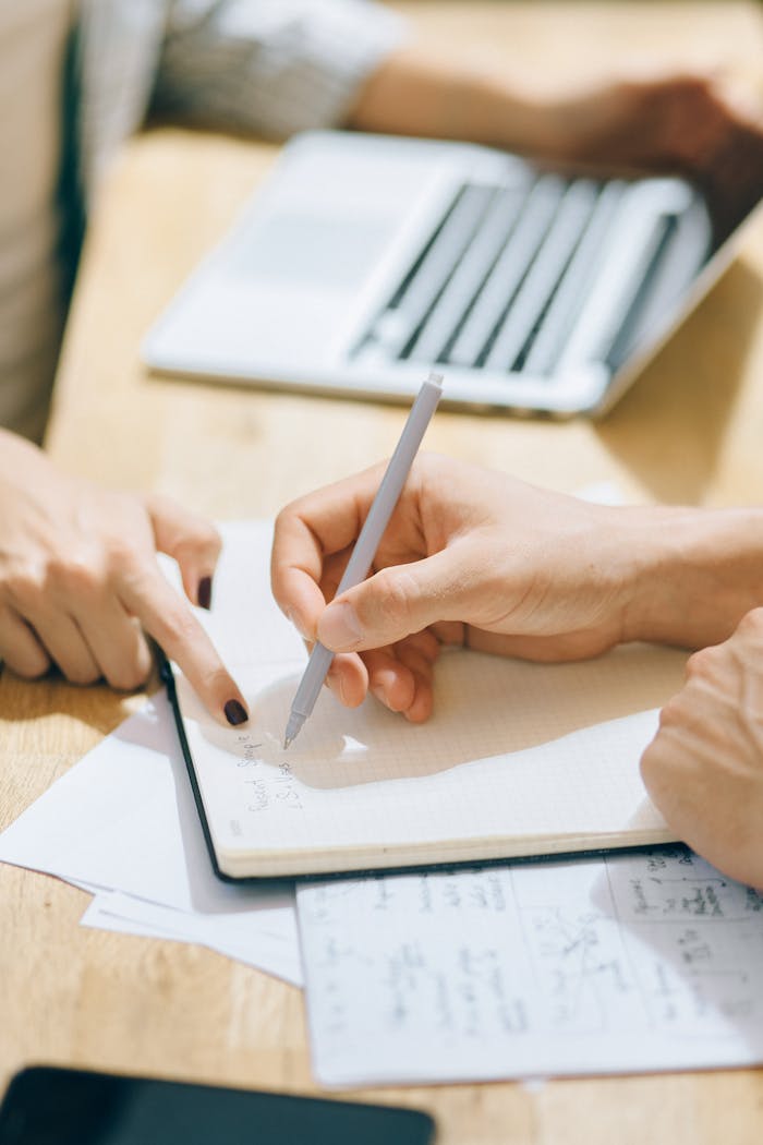 Two coworkers collaborating on a project in a modern office environment with a laptop and notebook.