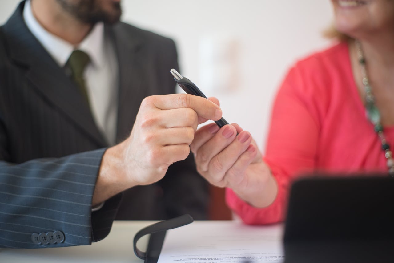 A man and woman exchange a pen during a business meeting indoors.
