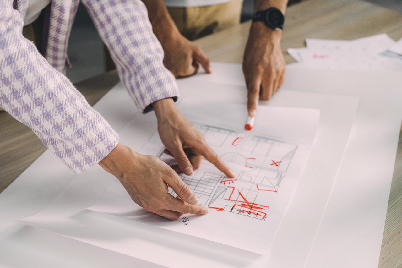 Two people discussing an architectural floor plan with red markings on paper.